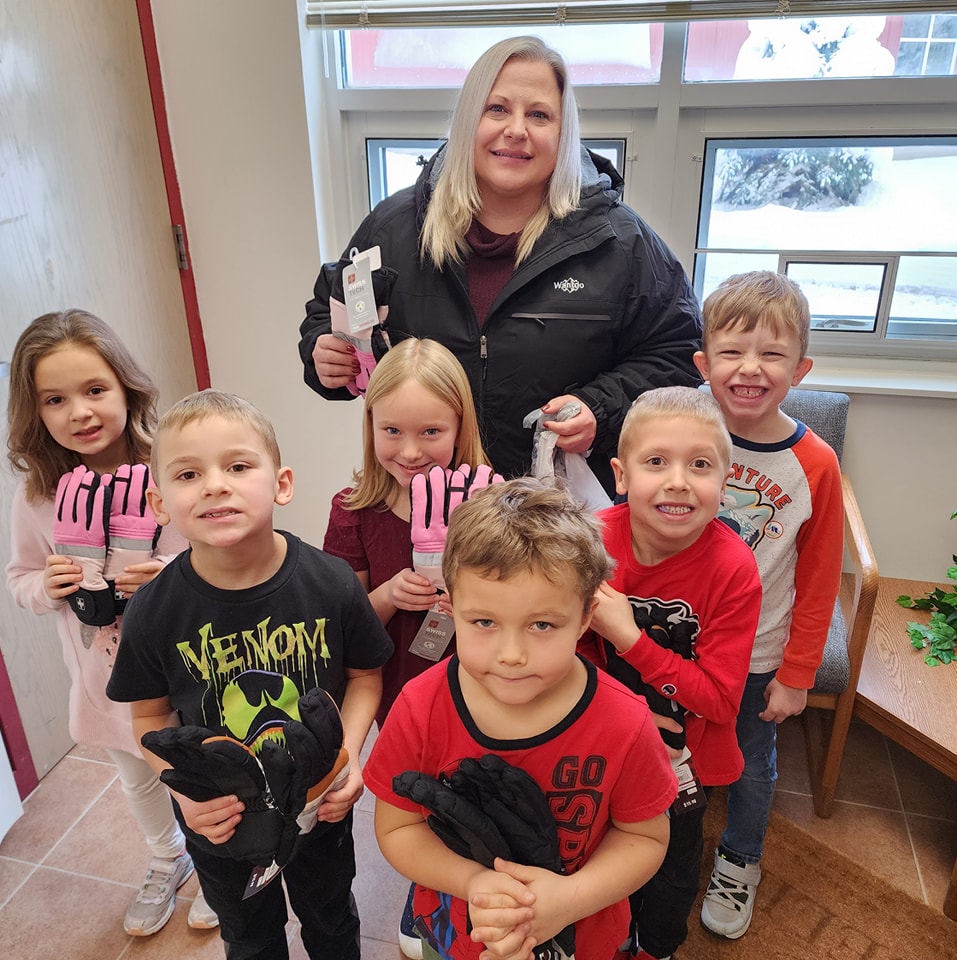 Bank Employee posing for a photo with kindergarten students holding up gloves donated to the class. 